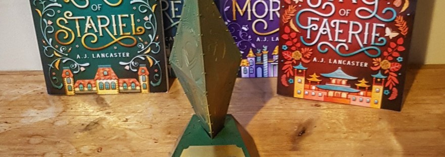 A gold and green trophy shaped like a diamond placed in front of the four books from the Stariel series.