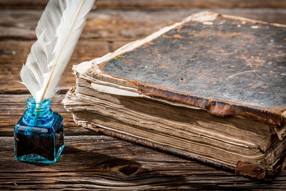 A photo of a feather quill and ink jar next to an old book