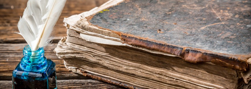 A photo of a feather quill and ink jar next to an old book